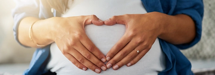 Pregnant woman with her hands on her belly, forming a heart shape with her fingers.