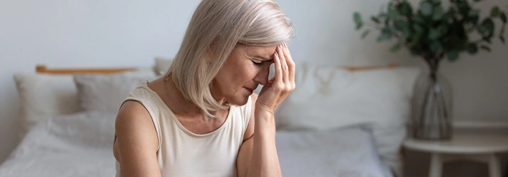 Woman sitting on the bed holding her forehead as if she had a headache